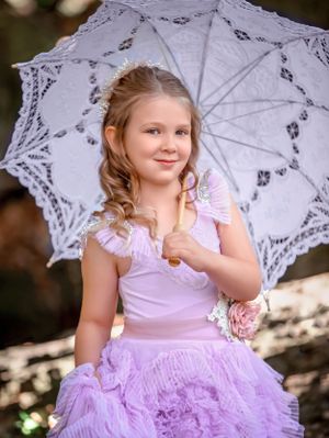 Smiling young girl in purple ruffle gown holding an open white lace parasol over her shoulder at John Oldham Park Perth.