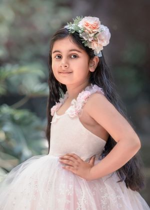 Beautiful girl with long dark hair smiling with hand on hip and wearing a floral headpiece and tutu style gown.