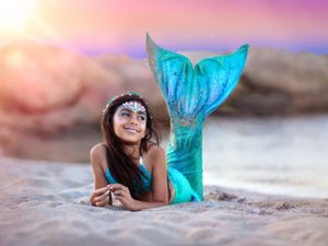 Young girl in mermaid costume at the beach lying on stomach, propped on elbows with tail in the air.