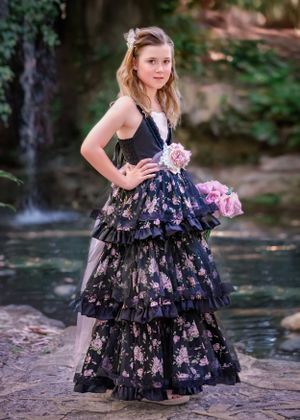 Preteen girl wearing a tiered black and pink floral gown standing in front of waterfall at John Oldham Park.