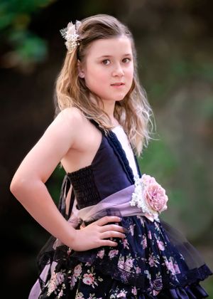 Girl wearing a pink and black floral gown with pink flower sash. Hand on hip looking directly at viewer.