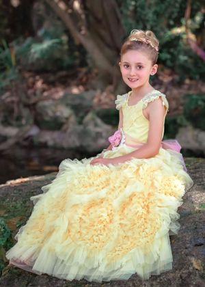 Girl in yellow ruffle gown smiling at the viewer while sitting on a boulder at John Oldham Park