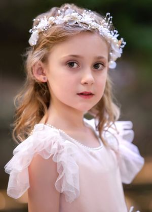 Portrait of a beautiful blonde haired child with large round eyes wearing a sparkly white beaded hair wreath.