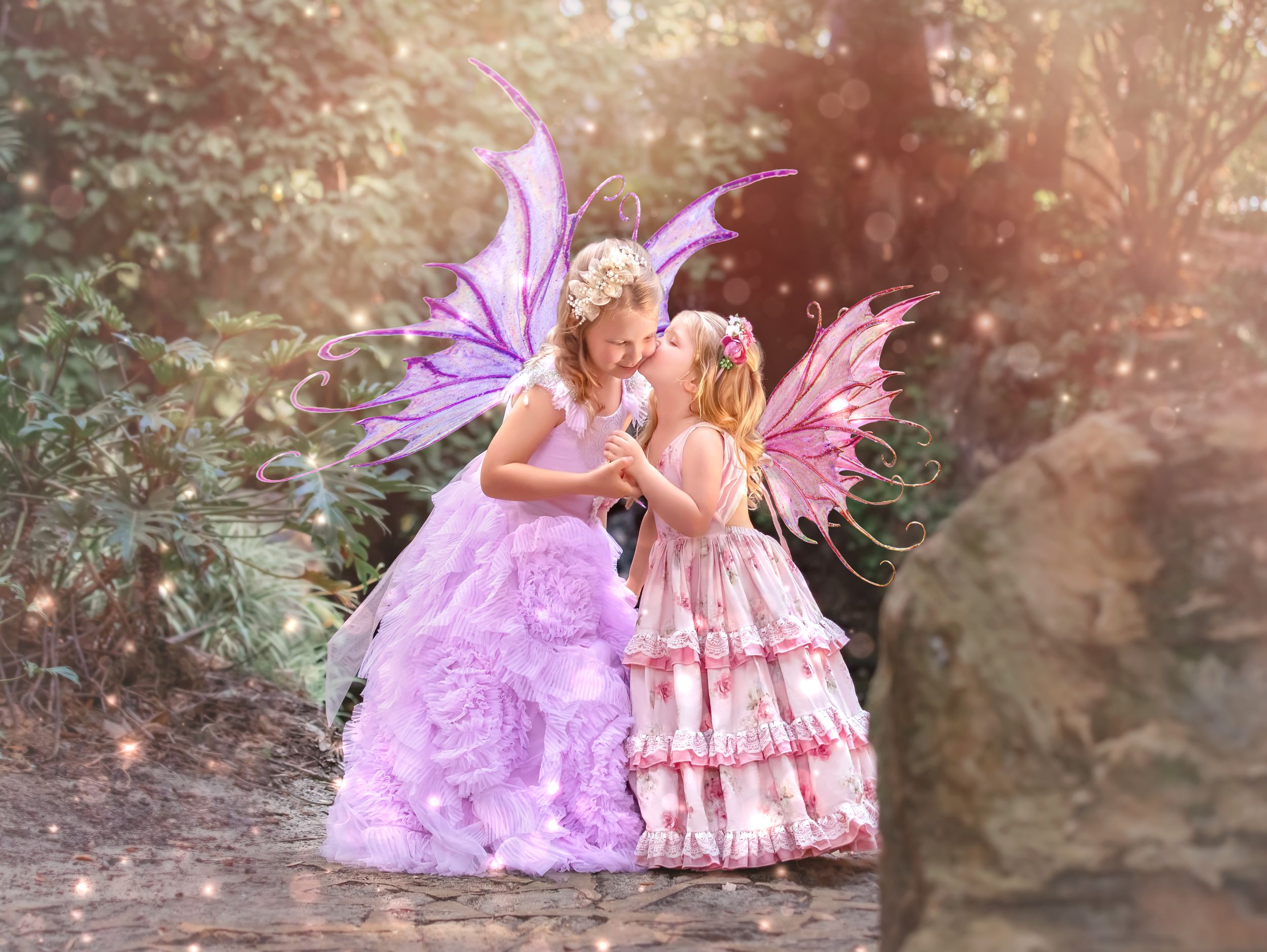 Two young sisters dressed in gowns with fairy wings standing in front of waterfall at John Oldham Park Perth.
