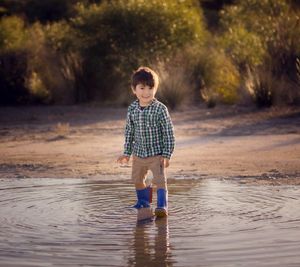 Small boy wearing dinosaur gumboots standing in a huge puddle in front of bushes at Rockingham Salt Lakes during sunset