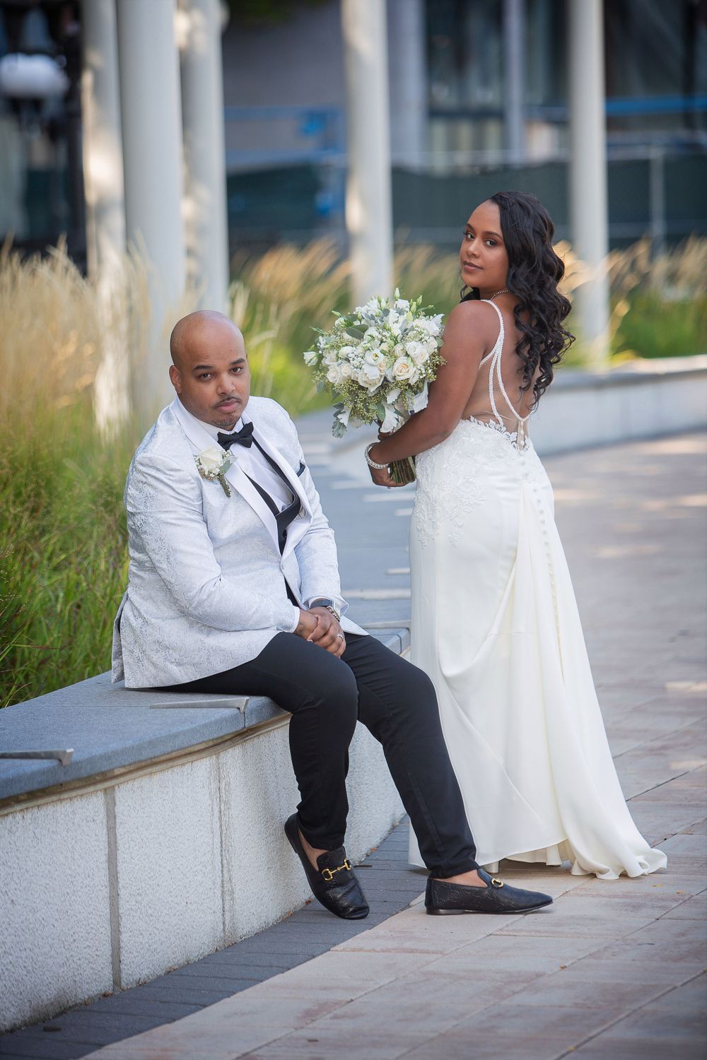 bride and groom sitting on the sidewalk in front of a building, in the style of nene thomas