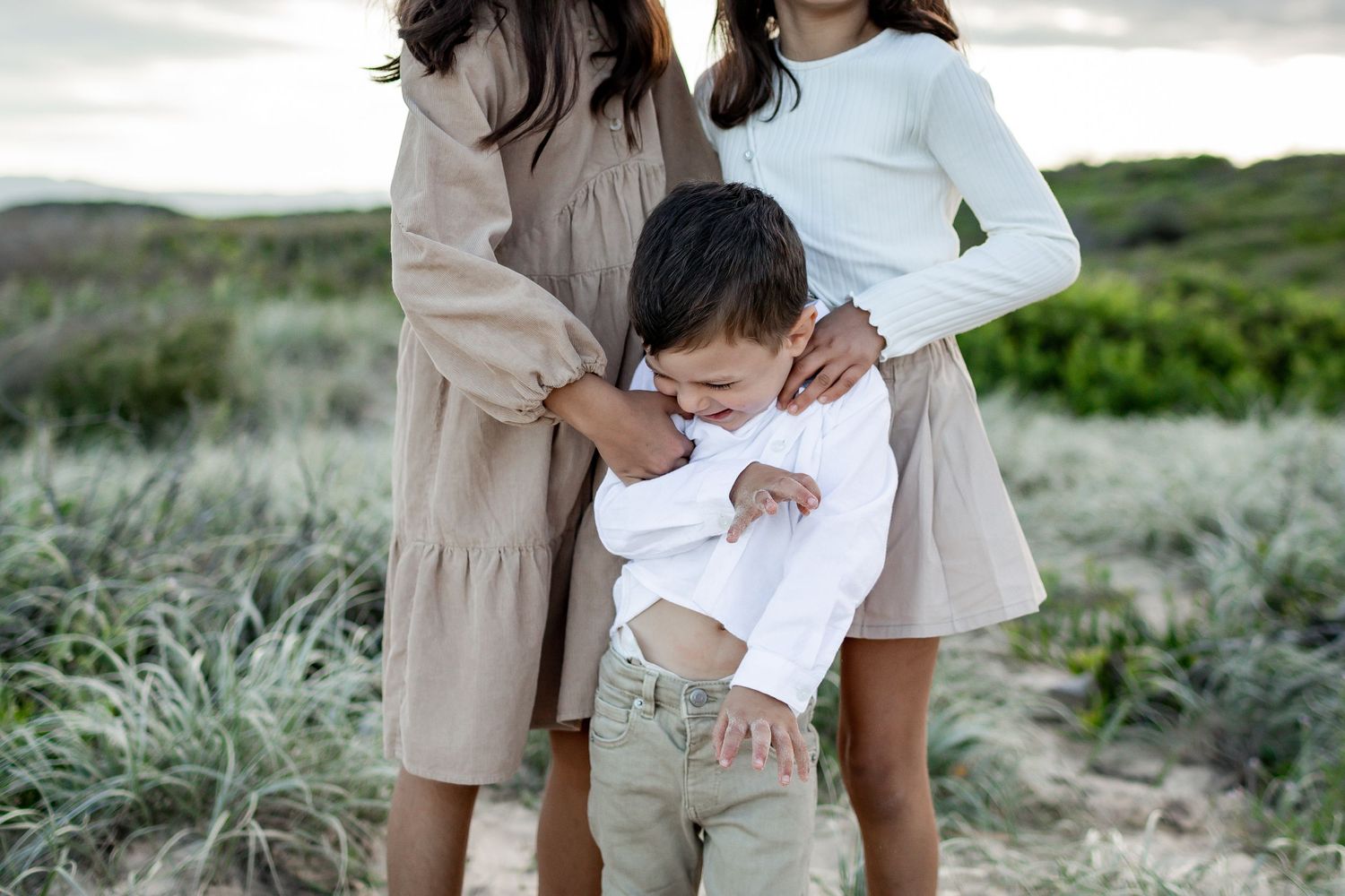 A playful family moment captured on coastal dunes with natural vegetation in the background.