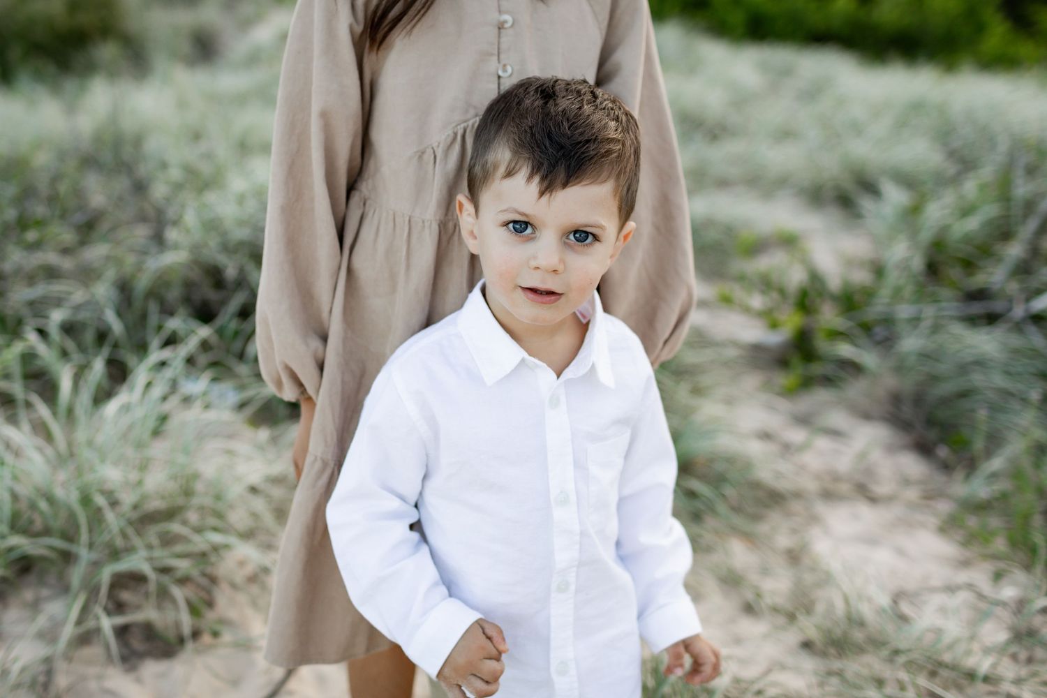 A child in a crisp white shirt poses against neutral coastal scenery.