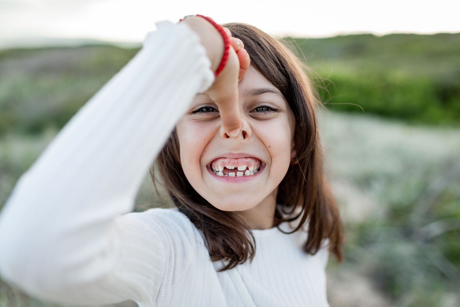 Child in white sweater laughing outdoors with windswept hair against natural landscape.