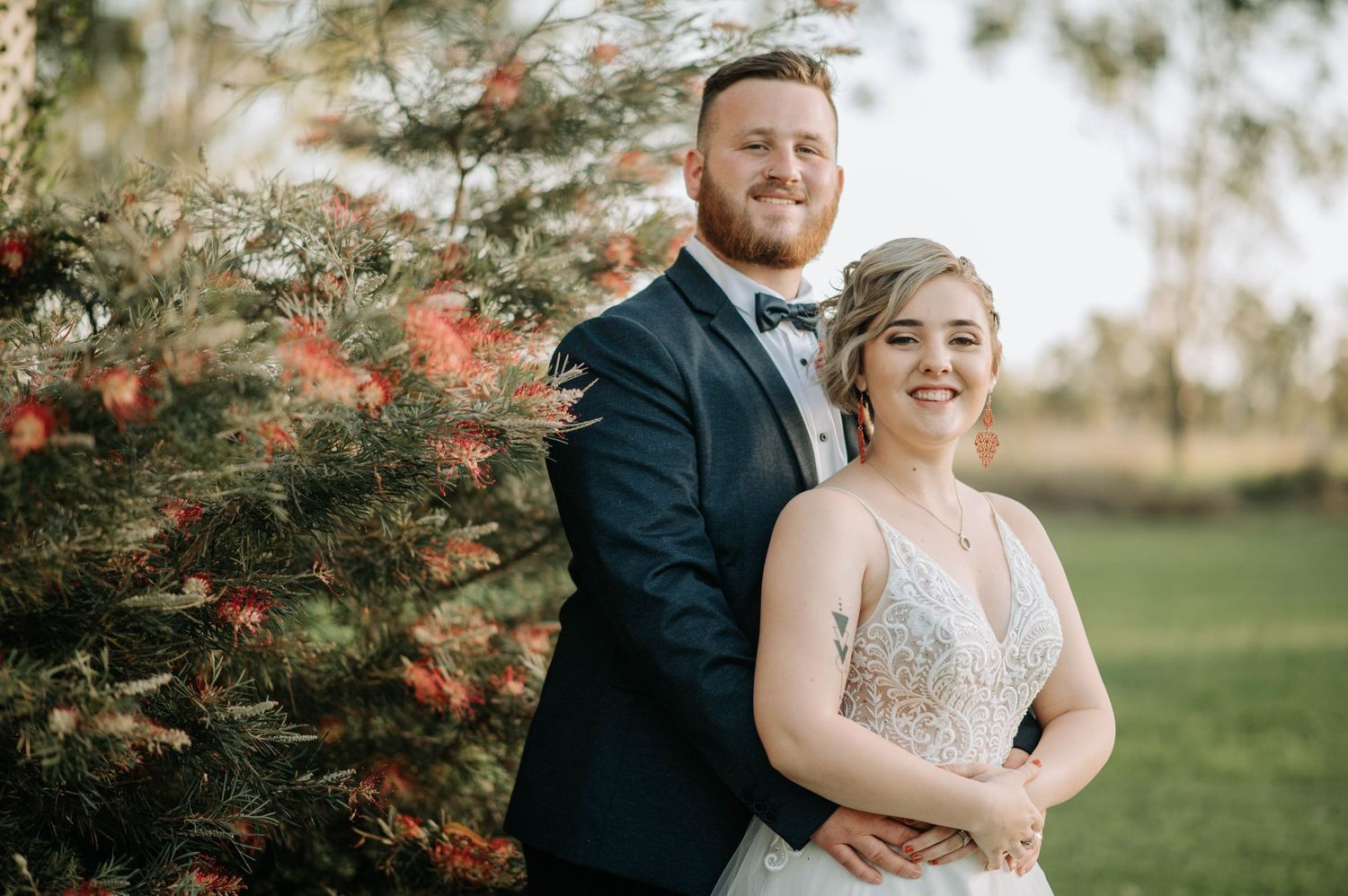 Wedding portrait with couple posed by flowering bush in afternoon light.