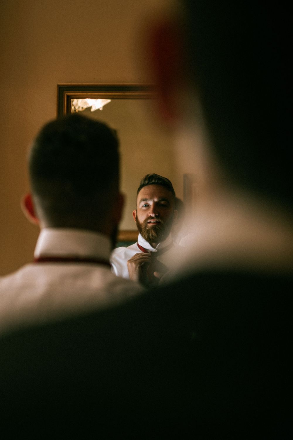Reflection in mirror shows someone adjusting their tie while getting ready.