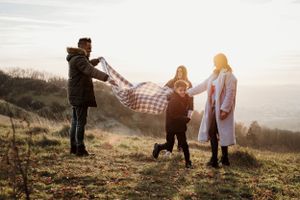 Playful family moments captured on a grassy hillside at sunset.