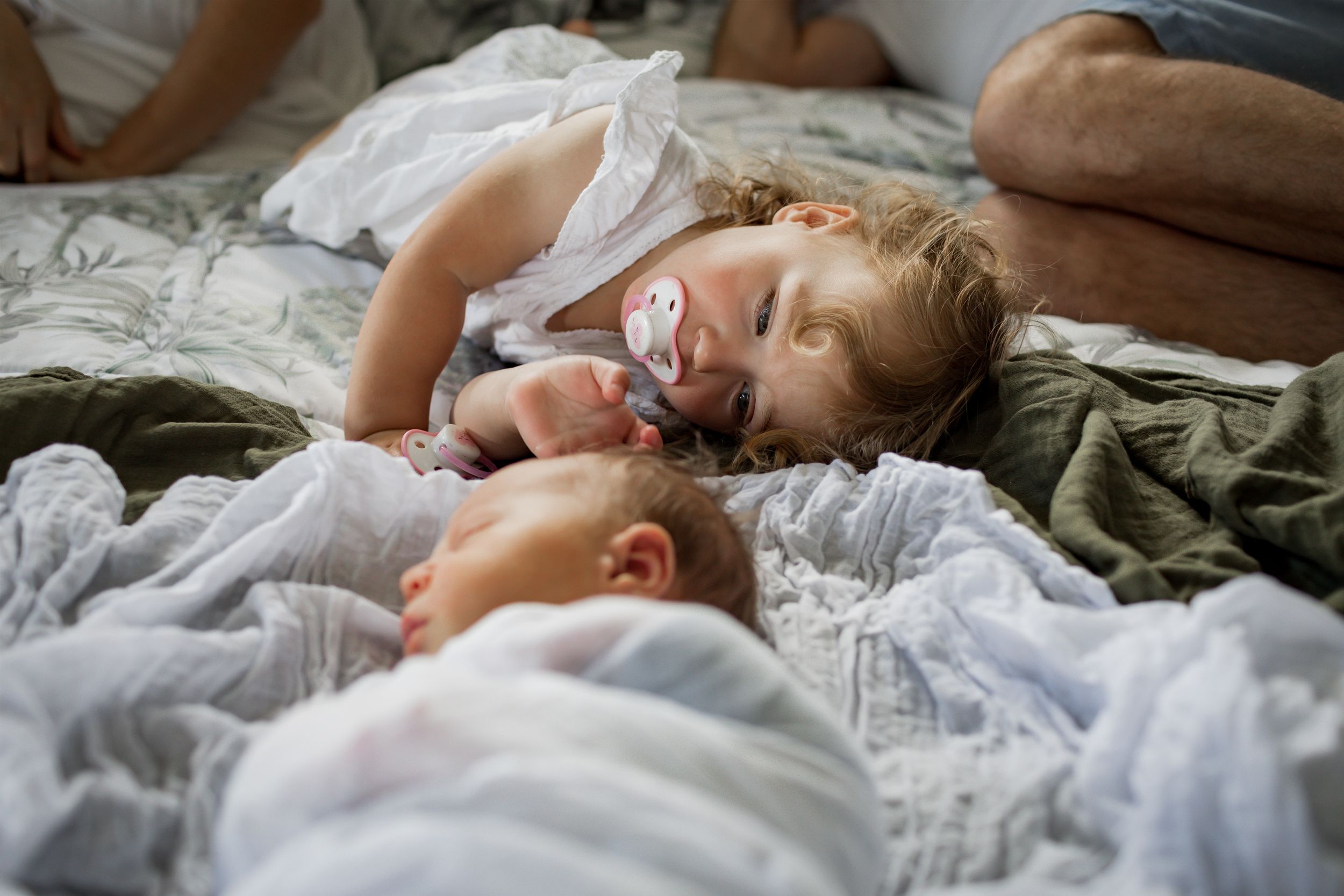 Toddler sleeping next to newborn sibling on white bedding.