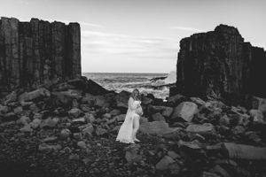 Woman in flowing dress standing between dramatic rock formations at the coast.