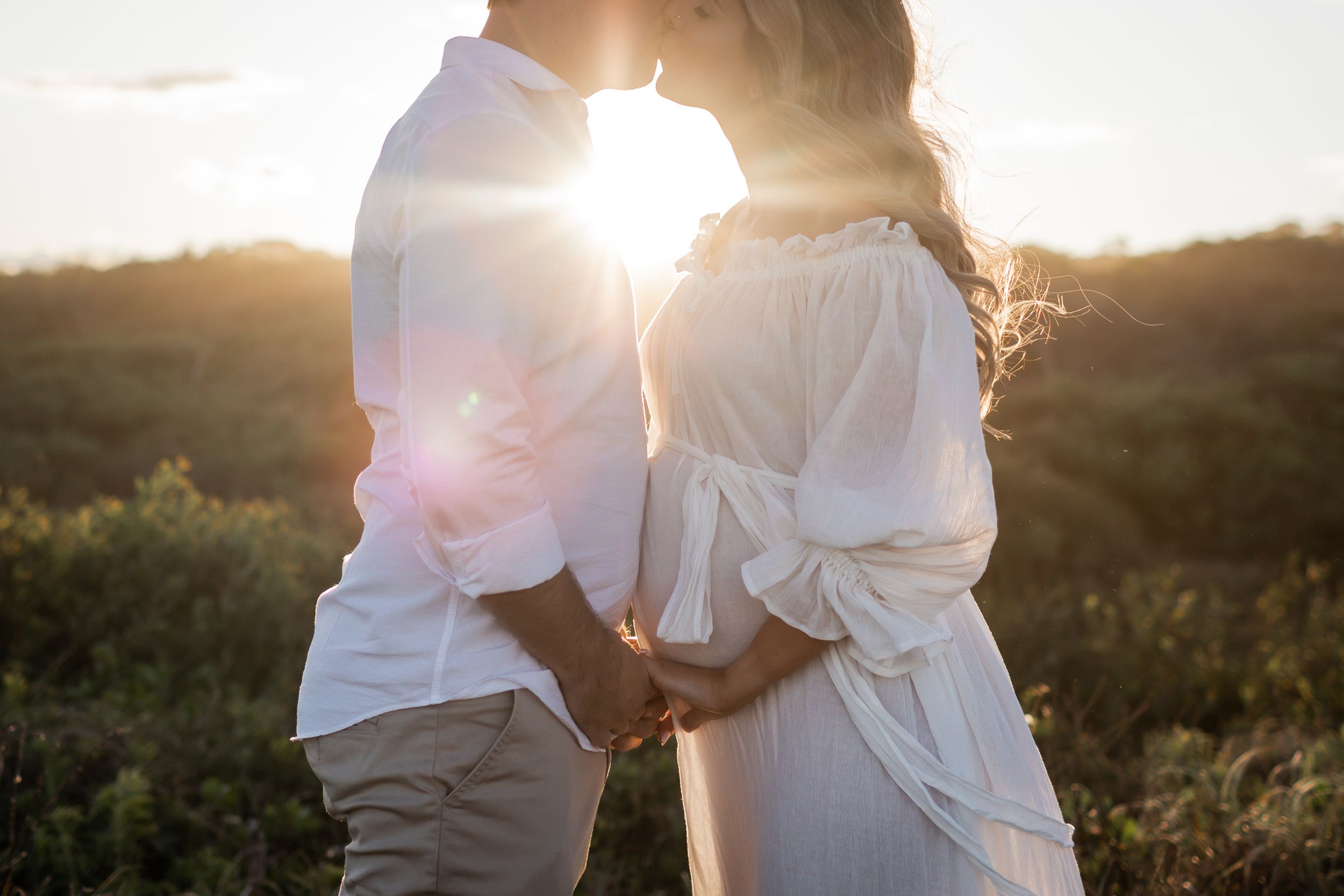 Romantic silhouette of couple embracing during golden hour with sun flare between them.