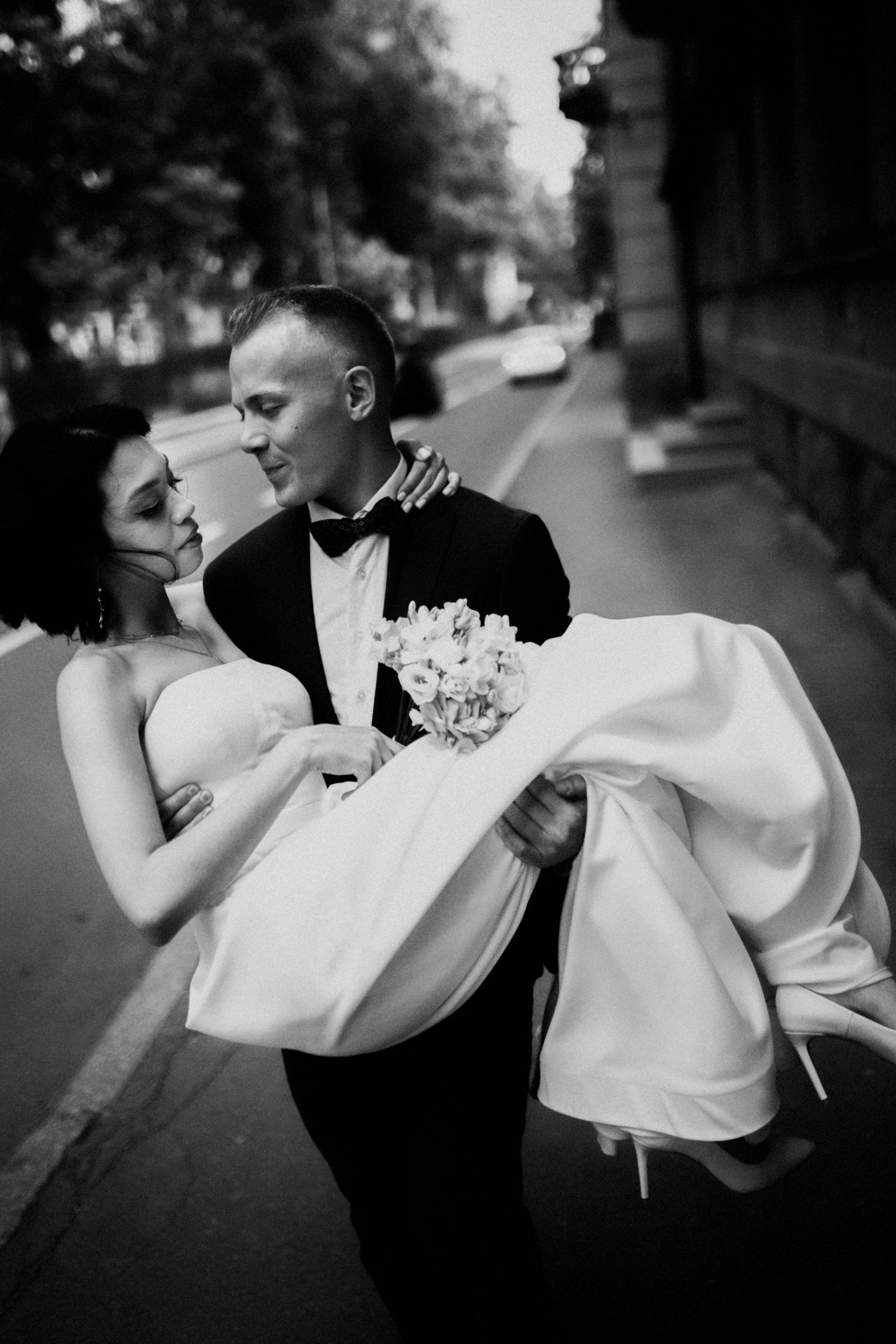 Romantic black and white wedding photo of couple in formal attire on city street.