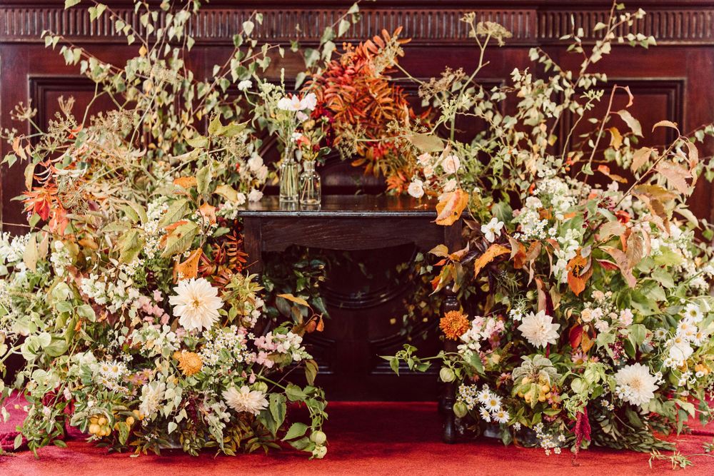 Luxurious floral arch with orange and white blooms against a dark red background.