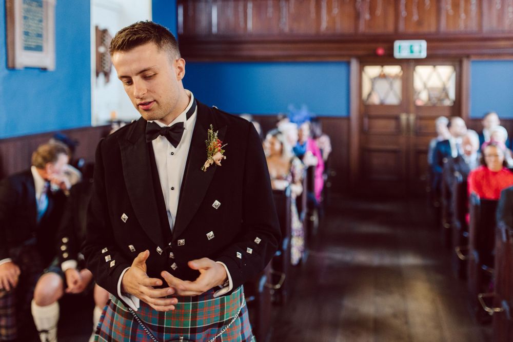 Traditional Scottish wedding ceremony in wood-paneled room with attendee in kilt and bow tie.