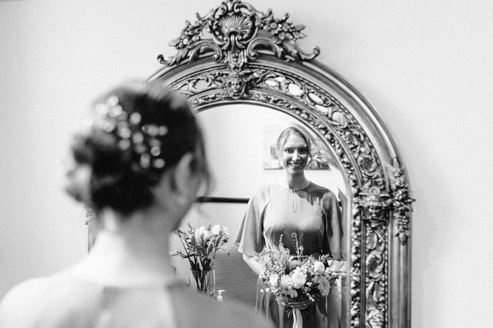An ornate vintage mirror with decorative silver frame reflects a wedding day preparation scene.