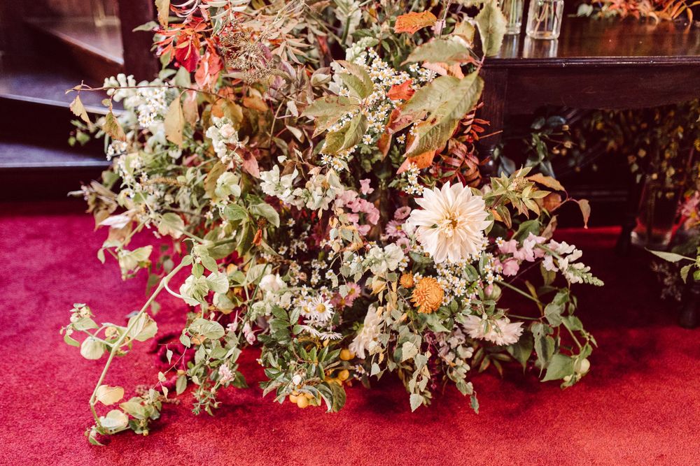 Rustic dried flower arrangement with pink and green foliage displayed on red surface.