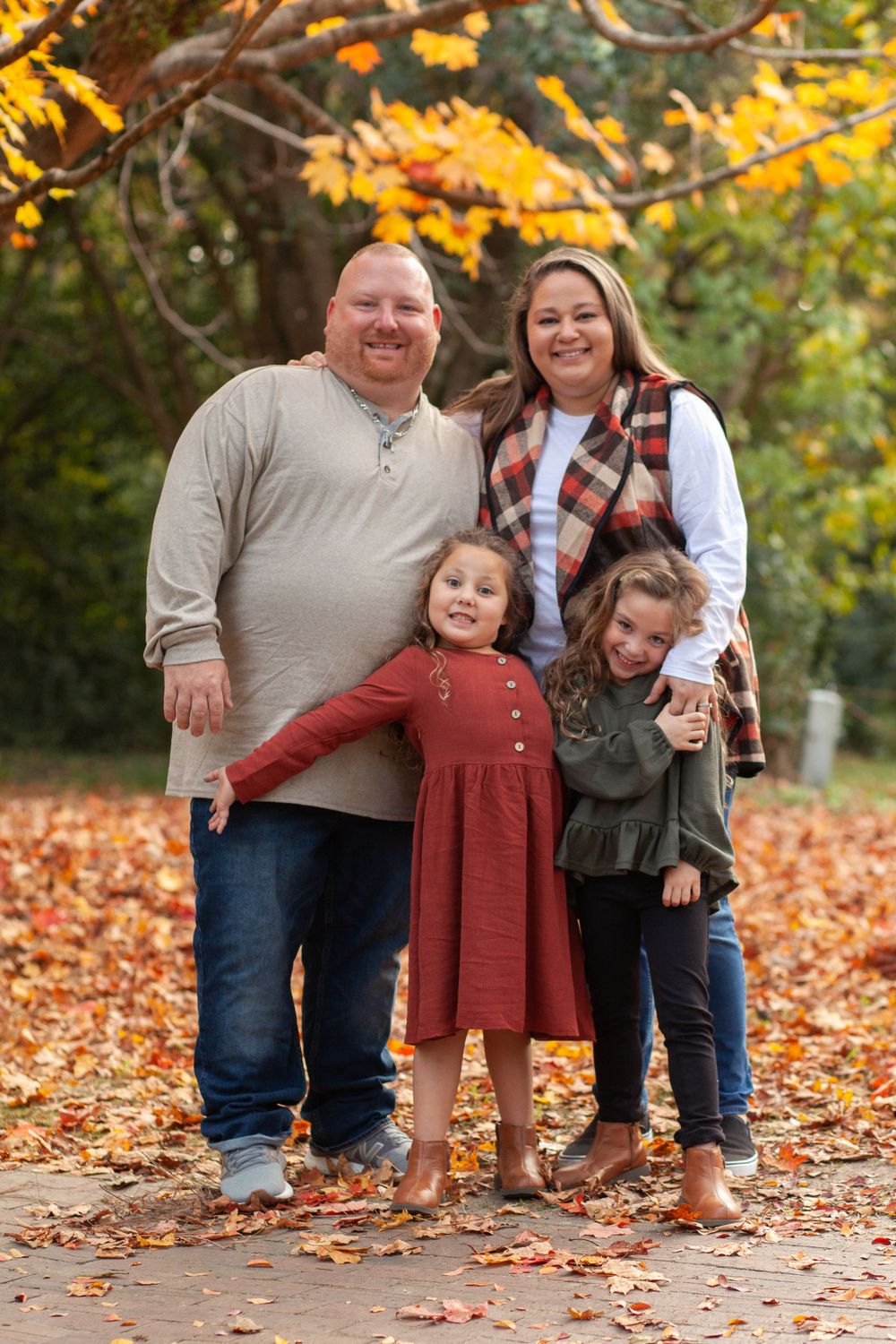 A family poses together on a path covered in fallen autumn leaves with golden fall foliage in the background.