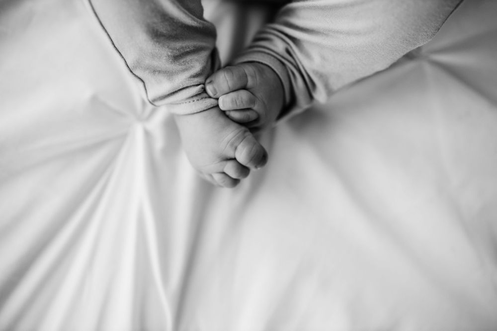 Black and white detail shot of tiny baby feet and fingers grasping on white fabric.