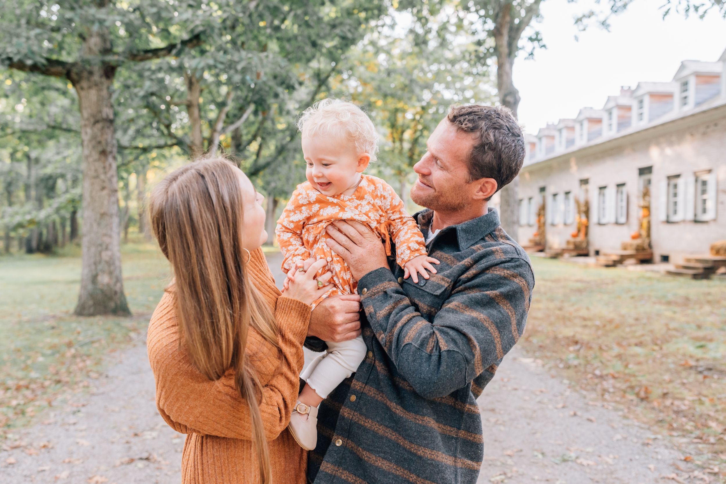 A mother and father hold onto their little girl and smile and laugh with her.