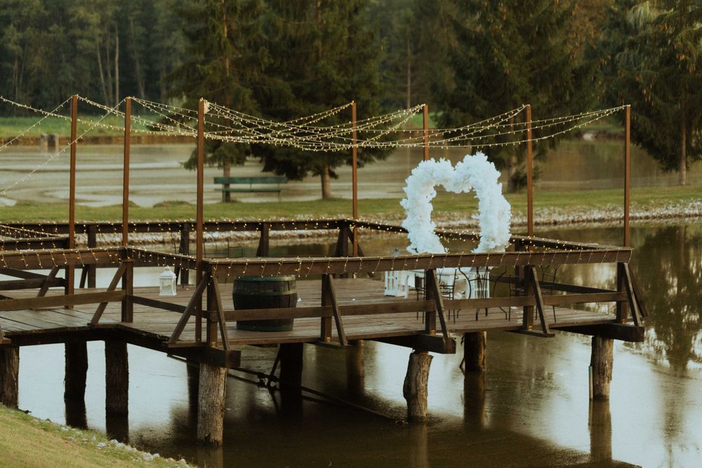 Rustic wooden bridge decorated with string lights and floral arch for outdoor wedding.