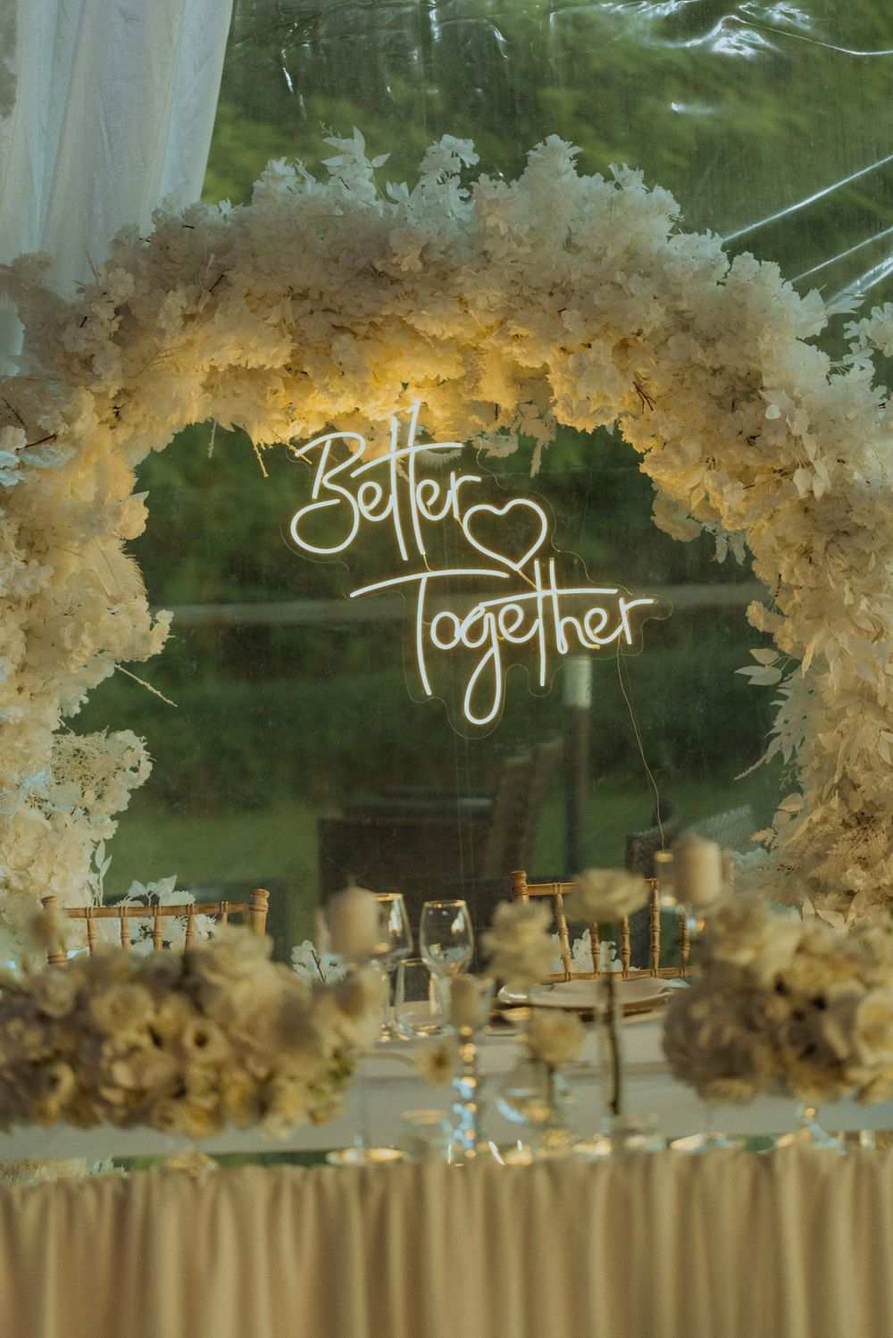 Elegant white floral arch with 'Better Together' neon sign for wedding reception decor.