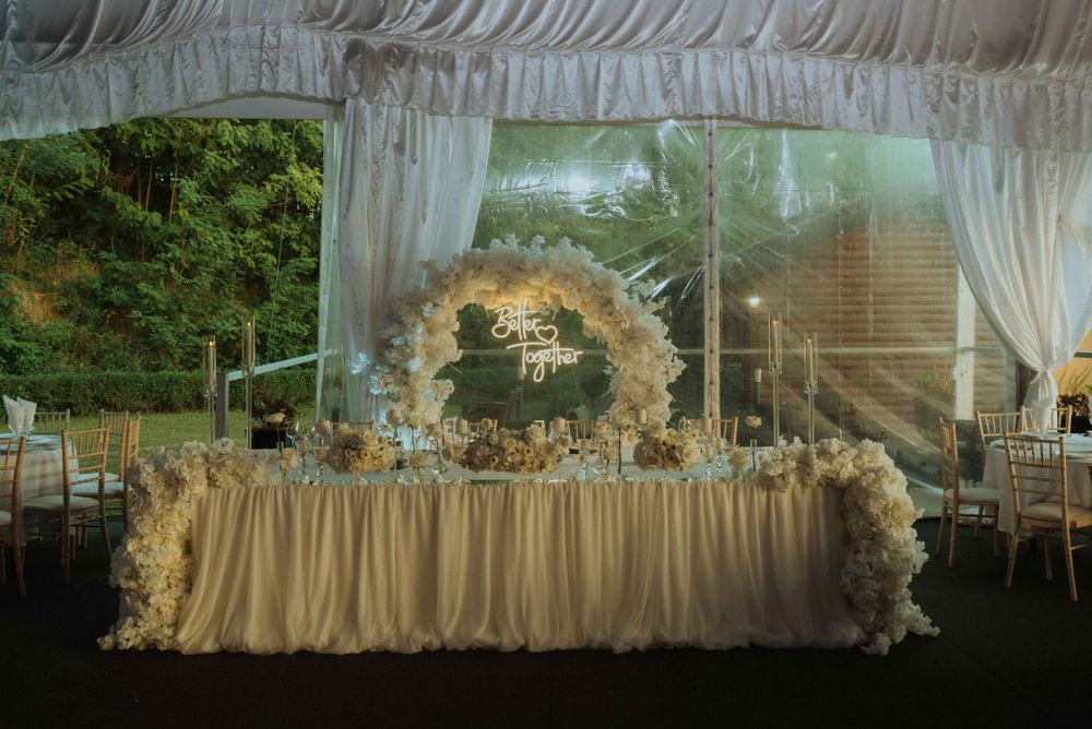 Rustic white wooden wedding welcome sign framed by evergreen branches.