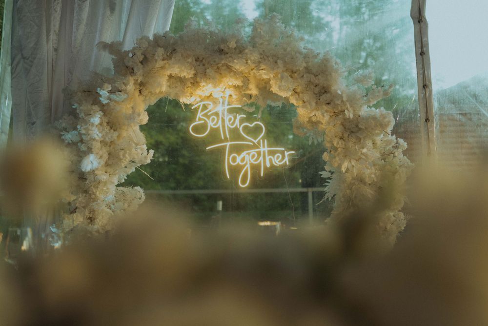 Wedding neon sign 'Better Together' surrounded by white floral arch decorations.