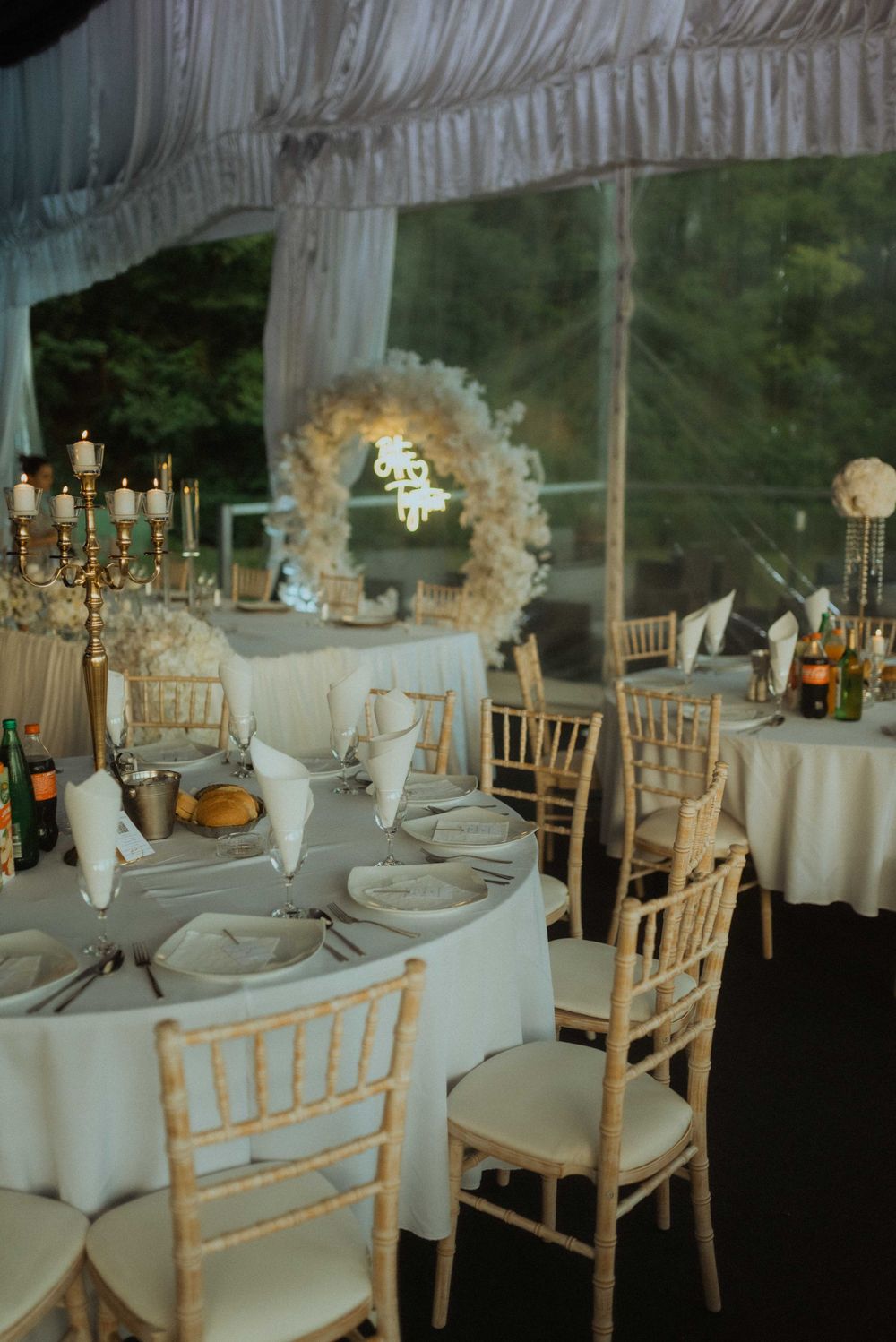 Elegant wedding reception setup with white linens, chiavari chairs, and floral arch decoration.