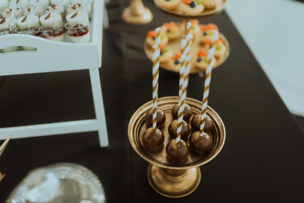 Golden dessert stand displaying chocolate cake pops at wedding reception.