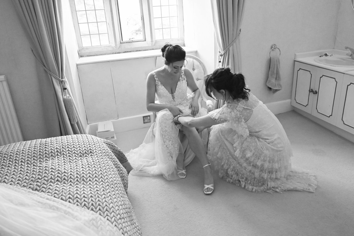 Black and white photo of wedding dress preparations in sunlit bedroom.
