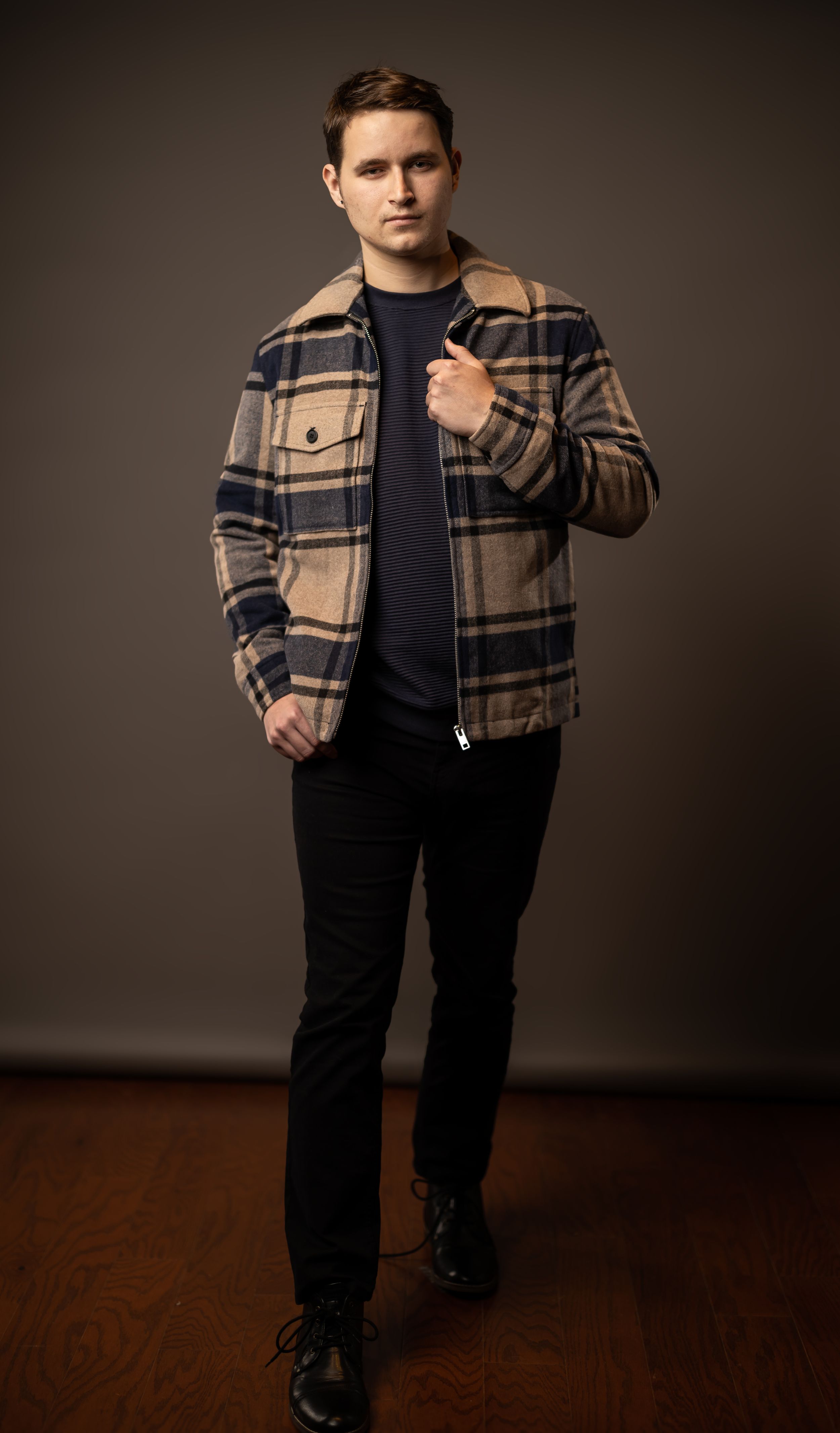 Fashion portrait showing person wearing plaid jacket and navy sweater on wooden floor.