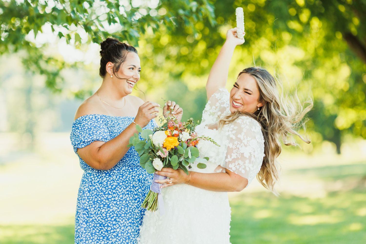 Wedding party members in blue dresses laugh and celebrate outdoors in natural sunlight.