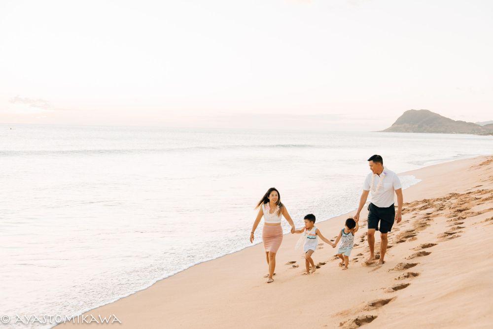 A family walks together leaving footprints in the sand along a scenic Hawaiian beach at sunset.