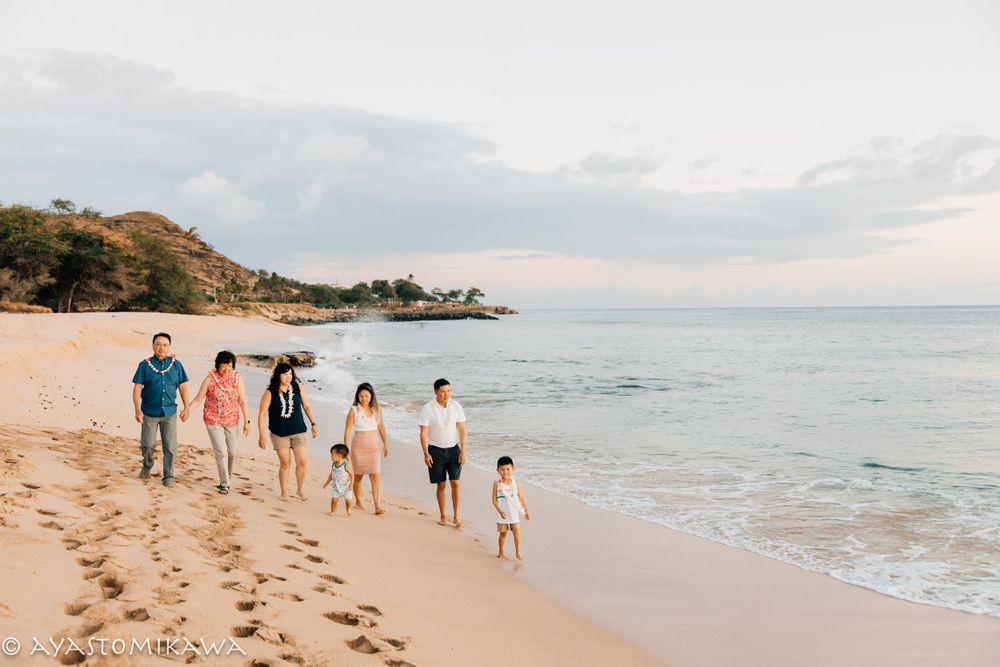 Multiple families stroll together on a Hawaiian beach during sunset, leaving trails of footprints in the sand.