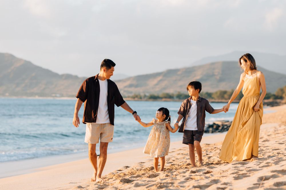 Family holding hands while walking along a sandy beach at sunset.