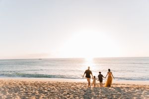 Silhouettes of people walking on beach at sunset with golden light reflecting on ocean.