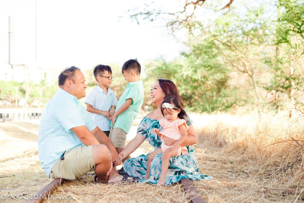 A family sits together in casual clothing against a natural outdoor backdrop with dry grass and trees.
