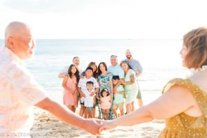 Extended group gathers on a scenic beach with ocean waves and blue sky in the background.