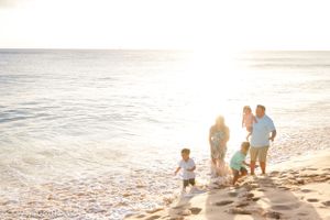 A group walks along the beach at sunset with golden light reflecting off the ocean.