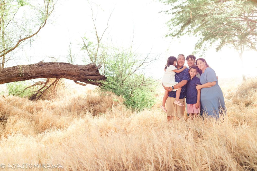 A group poses together near a large fallen tree branch in a golden field at sunset.