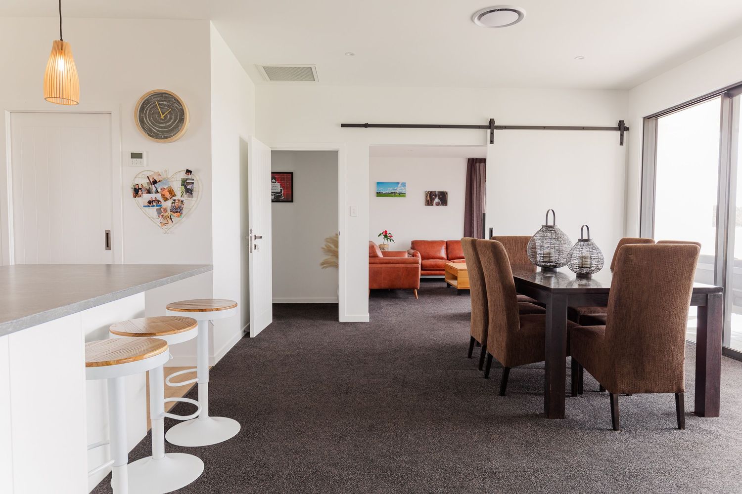 Modern open concept living area with bar seating, dining space and coral accent furniture on dark carpeting.