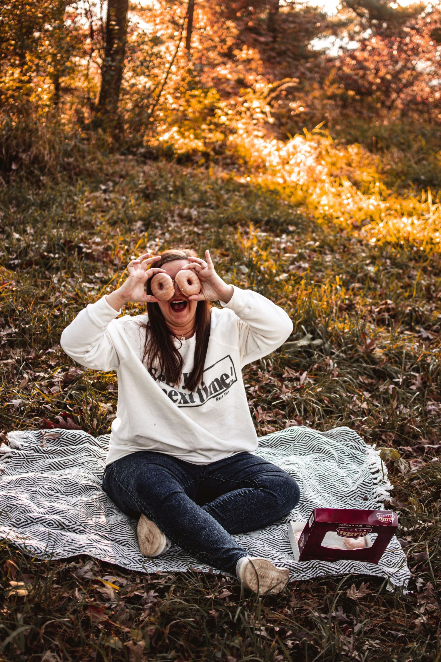 Person making playful gestures while sitting on blanket in fall forest with warm sunlight.