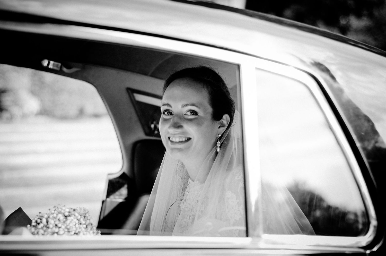 A beautiful bride smiles joyfully while sitting in the back seat of a classic car on her wedding day in Lugano.
