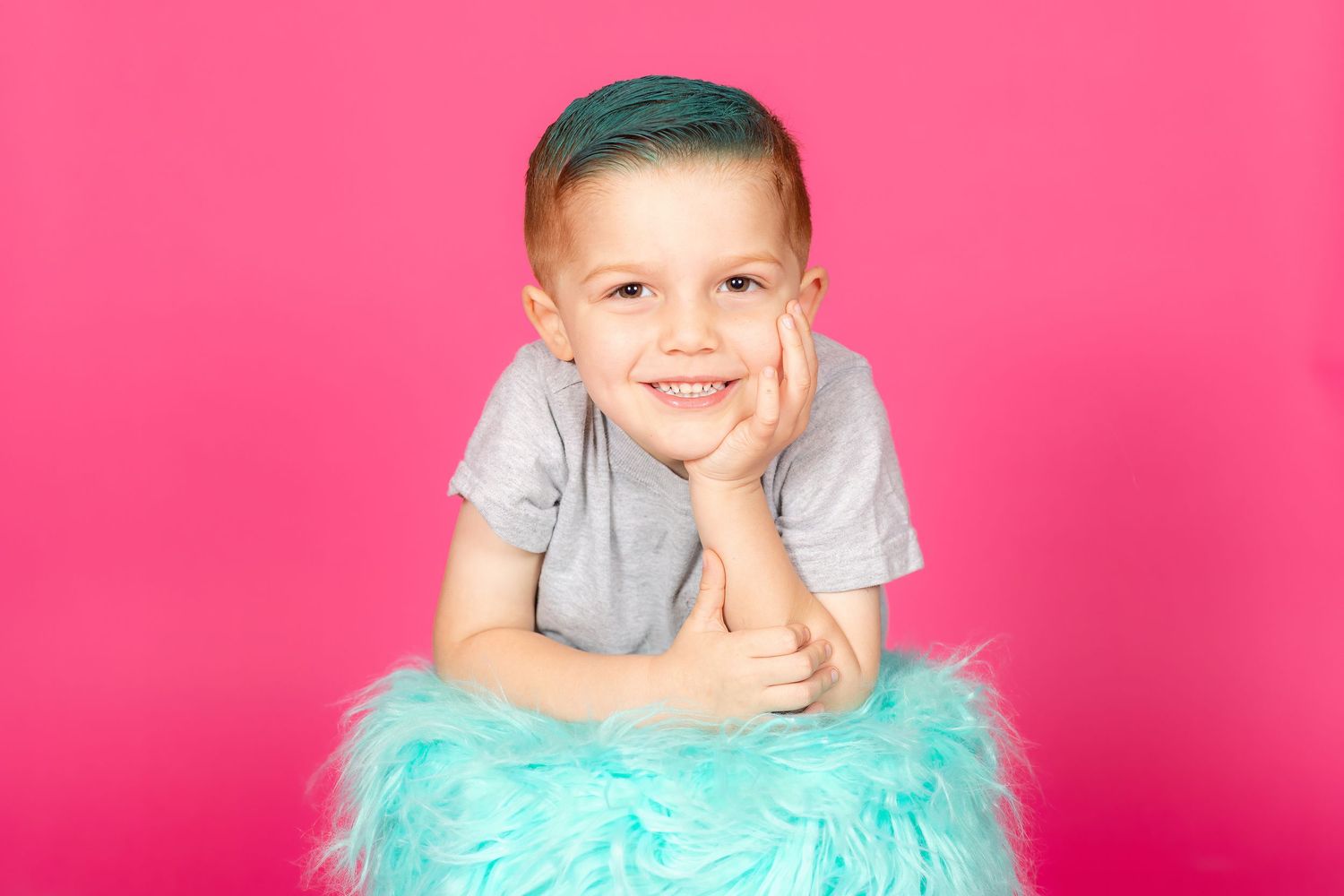 little boy with teal hair leaning on teal stool on savage tulip pink backdrop in studio in clayton new jersey