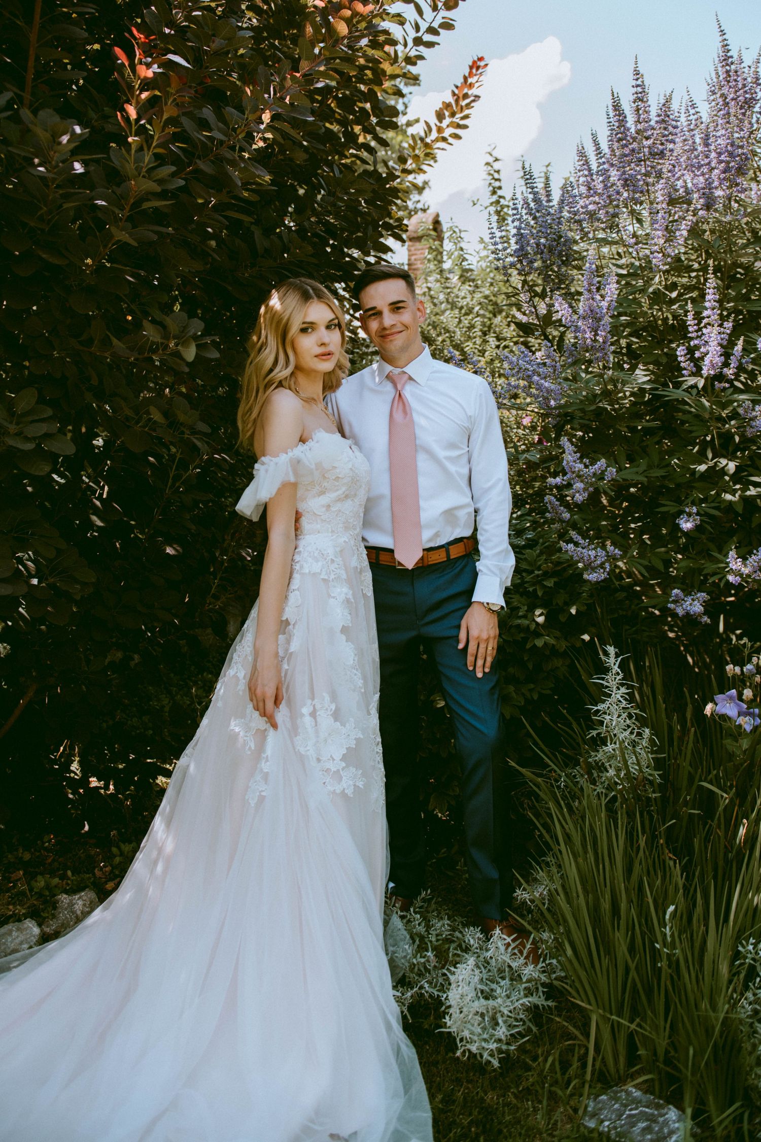 Bride and groom standing by flowers and trees in a romantic garden