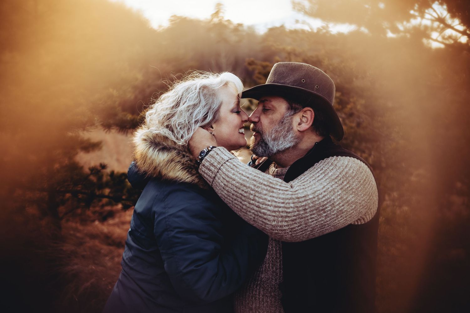 A tender moment between a couple wearing winter coats during golden hour.